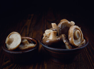 Delicious pickled mushrooms in clay cups stand on a wooden table . Salted mushrooms . Rustic food .