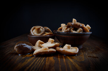 Delicious pickled mushrooms in cups and scattered on a wooden table . Rustic food .
