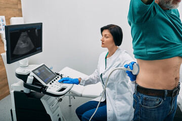 Male patient getting kidneys sonography exam standing near ultrasound specialist and ultrasound...