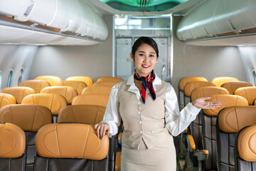 Asian flight attendant posing with smile at middle of the aisle inside aircraft for welcoming...