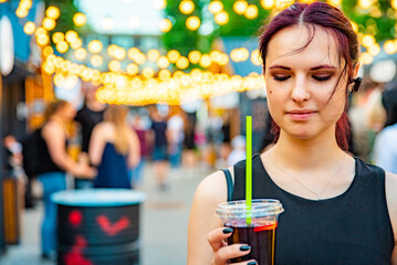 young woman holding a plastic glass with a drink on the street