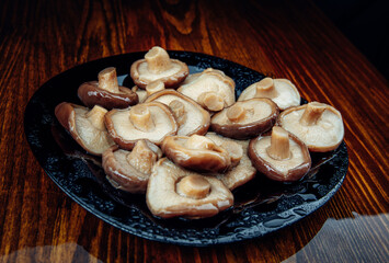 Beautiful pickled mushrooms in a black glass plate . Healthy village food . Pickled black milk mushroom .