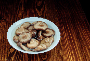 A white plate with pickled mushrooms stands on a wooden table . Healthy village food .