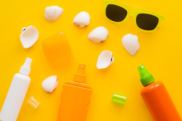 Top view of seashells near sunscreens and sunglasses on yellow background.