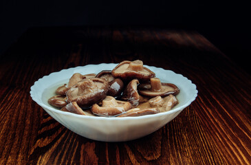 A white plate with pickled mushrooms stands on a wooden table side view . Healthy village food .