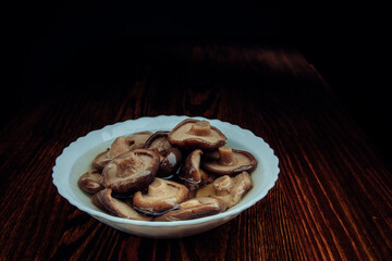 A white plate of pickled mushrooms . Healthy village food . Pickled black milk mushroom .