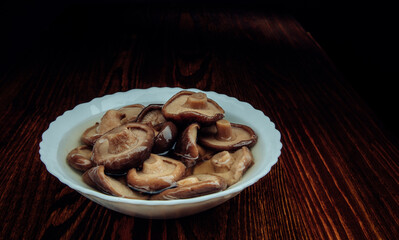 A white plate of pickled mushrooms . Healthy village food . Pickled black milk mushroom .