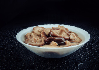 A white plate of pickled mushrooms . Healthy village food . Pickled black milk mushroom .