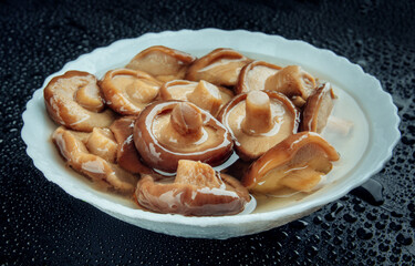 A white plate of pickled mushrooms . Healthy village food . Pickled black milk mushroom .
