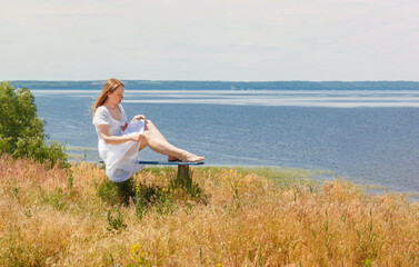 Naklejka na ściany i meble A beautiful girl sits on benches on the seashore with a view of the sky