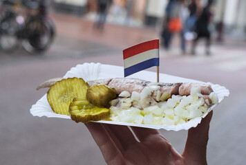 Traditional Dutch street food - saline herring with pickles, onions and Dutch flag in a fish. Still...