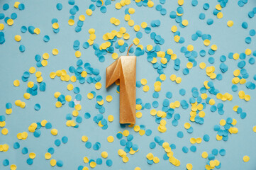 Number 1 one golden celebration birthday candle on yellow and blue confetti Background. One year...