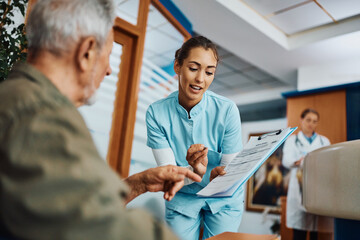 Young nurse assisting senior man in filling paperwork at doctor's office. - Powered by Adobe