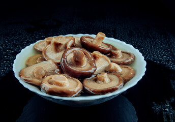 Salted mushrooms in a plate on a black background . Pickled black milk mushroom .