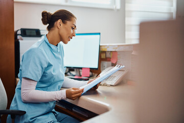 Obraz na płótnie Canvas Young nurse going through medical records at reception desk in hospital.