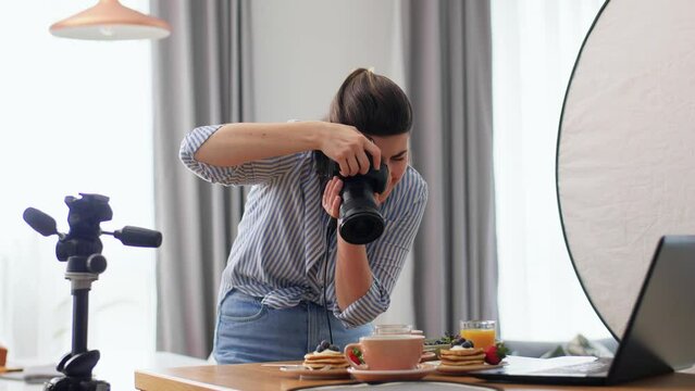 blogging, profession and people concept - female food photographer with camera photographing pancakes, coffee and orange juice in kitchen at home