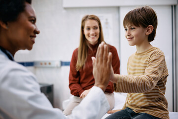 Happy boy giving high five to his pediatrician at medical clinic.