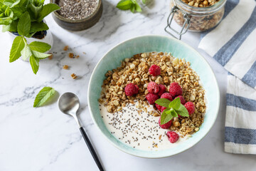 Breakfast, sweet dessert. Diet nutrition concept. Homemade granola with yogurt, chia seeds and raspberry on a marble tabletop.