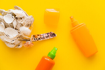 Top view of seashells with found at sea lettering near sunscreens on yellow background.