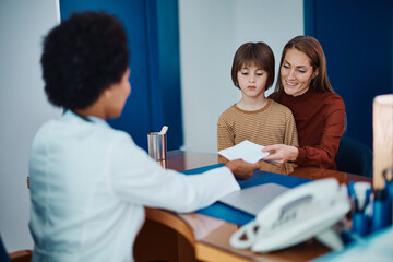 Happy mother receives prescription from pediatrician after son's medical exam at doctor's office.