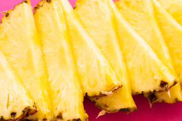 Close up view of cut fresh pineapple on pink surface.