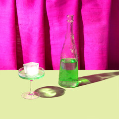 Tall champagne glass, ice cube and green drink, neon pink shantung silk drapery background. Creative summer refreshment arrangement. 