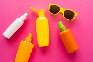 Top view of bottles of sunscreens near sunglasses on pink surface.