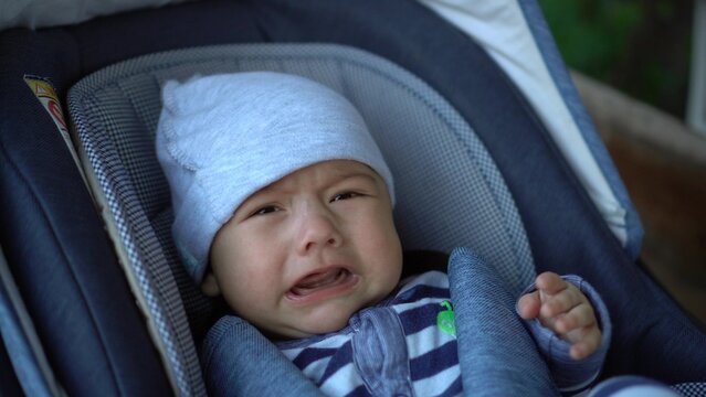 A newborn baby is crying while lying in a stroller. The child is unwell.