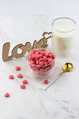 A bowl of breakfast cereal, a glass of milk and a wooden love inscription on a white table. Romantic breakfast