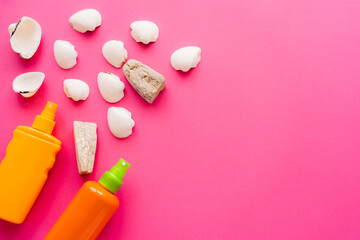 Top view of seashells and sunscreens on pink background.