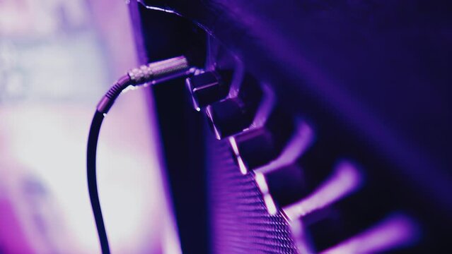 The plug of the wire is inserted into a guitar amplifier standing on stage at a rock concert. Shooting in close-up