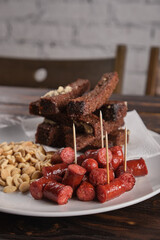 Beer appetizer assorted salted peanuts, sausages and croutons with garlic in a plate on a wooden table. Vertical orientation, close-up, no people, copy space