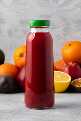 Various fruits and freshly squeezed fruits juice in bottle on gray background