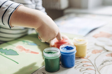 Fototapeta na wymiar Finger painting. Cute little boy painting with fingers at home. Close-up of child's hand in colorful paints. Early education concept. Sensory play. Development of fine motor skills.