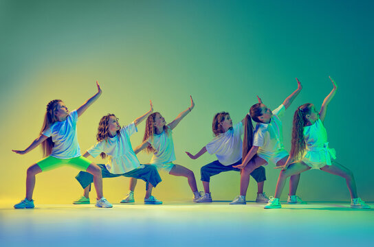 Group of children, little girls in sportive casual style clothes dancing in choreography class isolated on green background in yellow neon light. Concept of music, fashion, art