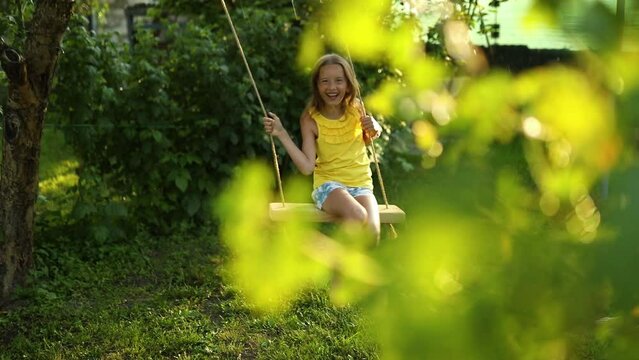 Happy barefoot laughing child girl swinging on a swing in sunset summer day on the backyard at home, summertime outdoor, vacation.