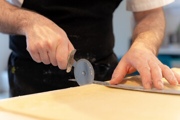 Detail of a man's hands cooking homemade croissants, measuring the puff pastry and making cuts, work at home