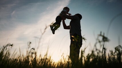 father playing with son in the park. happy family kid dream concept. father throws baby up silhouette in summer at sunset. parent and child play toss up silhouette outdoors lifestyle in the park