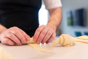 Hands of a man cooking small croissants at home, shaping with the puff pastry