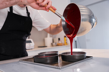 Hands of a man cooking a red velvet cake at home, adding the sponge cake in the molds before...