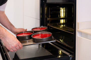 Hands of a man cooking a red velvet cake at home, putting the red cake in the oven, work at home