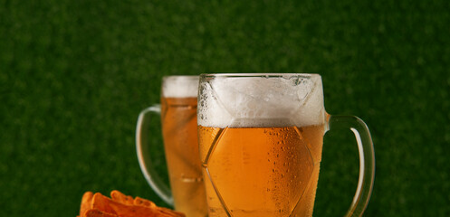 Two glasses of beer with soccer ball on the green grass background.