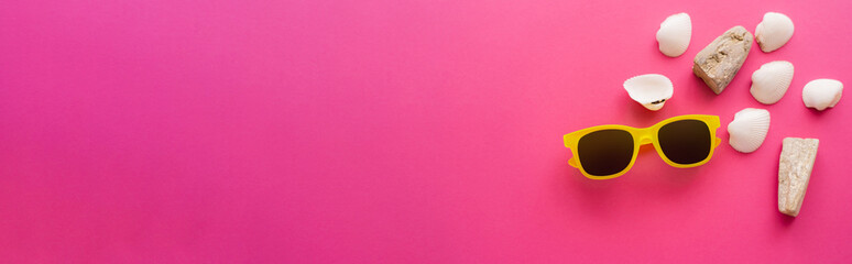 Top view of sunglasses and seashells near copy space on pink background, banner.