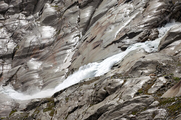 Fototapeta na wymiar Source of Rhone river, rough water fall between mountain rocks. High alps landscape of arid terrain with waterfall.