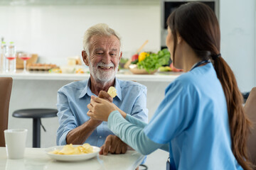 Caring Asian nurse take care of senior elderly man to don't eat junk food at hospital. Friendly...