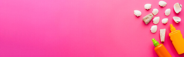 Top view of seashells and bottles of sunscreens on pink background, banner.