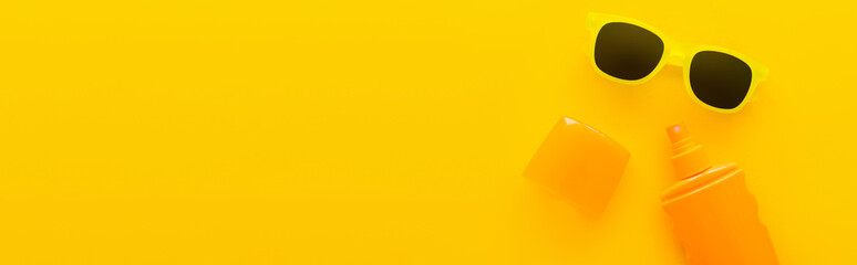 Top view of sunscreen and sunglasses on yellow background, banner.