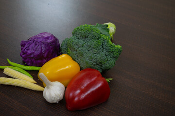 Picture of sautéed salad on a white plate along with healthy raw boiled exotic vegetables. baby corn, capsicum, bell pepper, broccoli, garlic, chilly, cabbage, tomato, onion, carrot on wooden table.