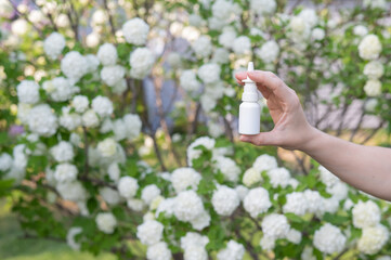 Woman's hand with a nasal spray on a background of a flowering tree. 
