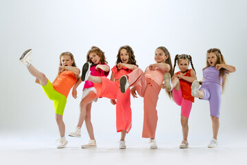 Dance group of happy, active little girls in bright colorful clothes dancing isolated on white...